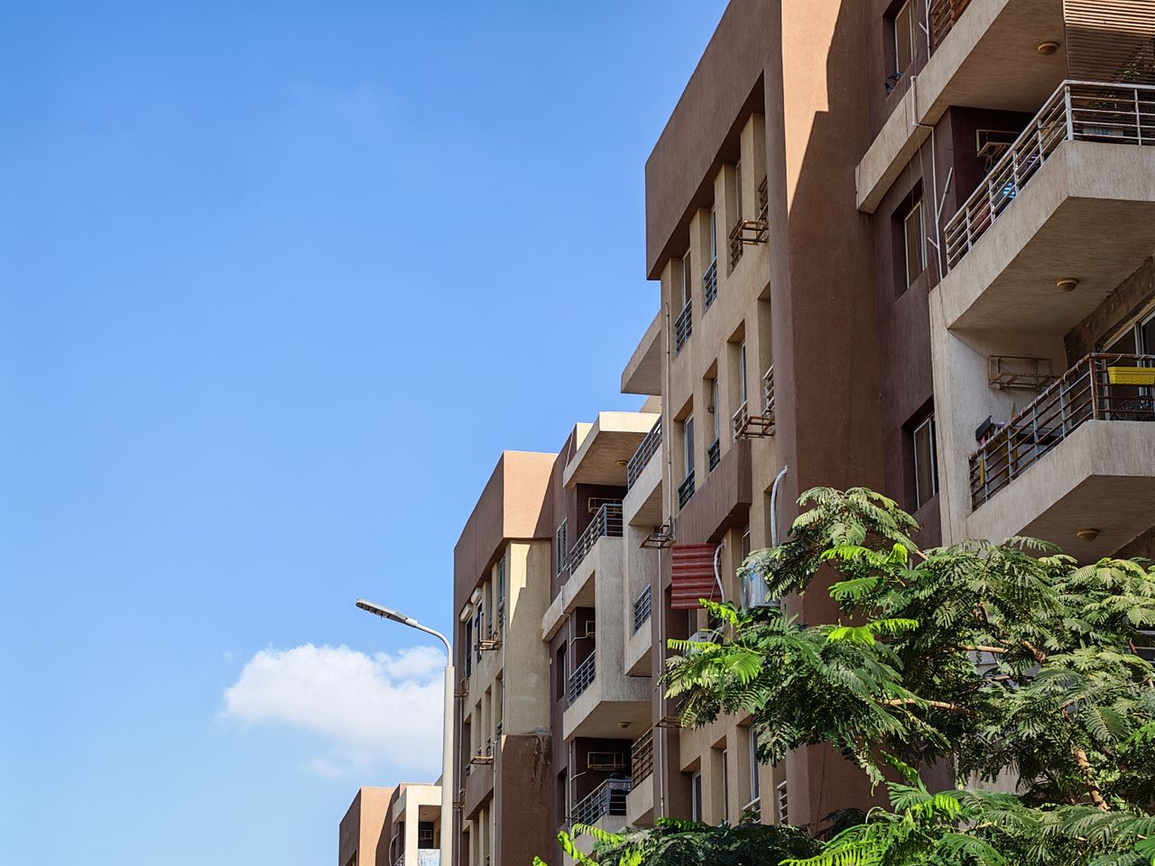 Urban apartment building against a bright blue sky with foliage in the foreground.