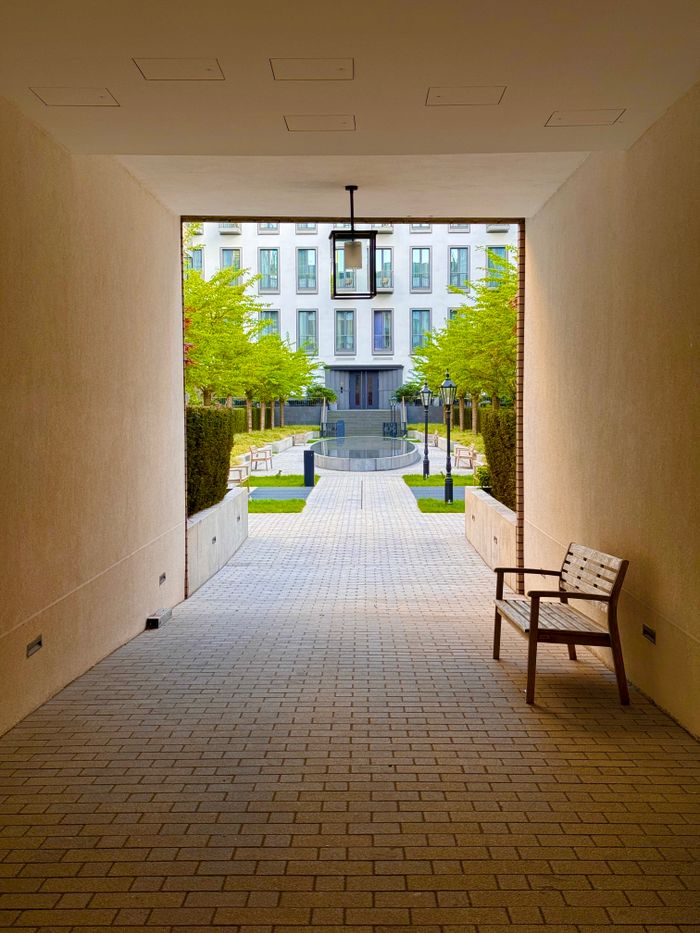 A serene view through a covered passageway leading to a tranquil courtyard with benches and green trees.